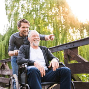 Man in a wheelchair enjoys a summer day on a boardwalk while a younger man pushes the wheelchair.